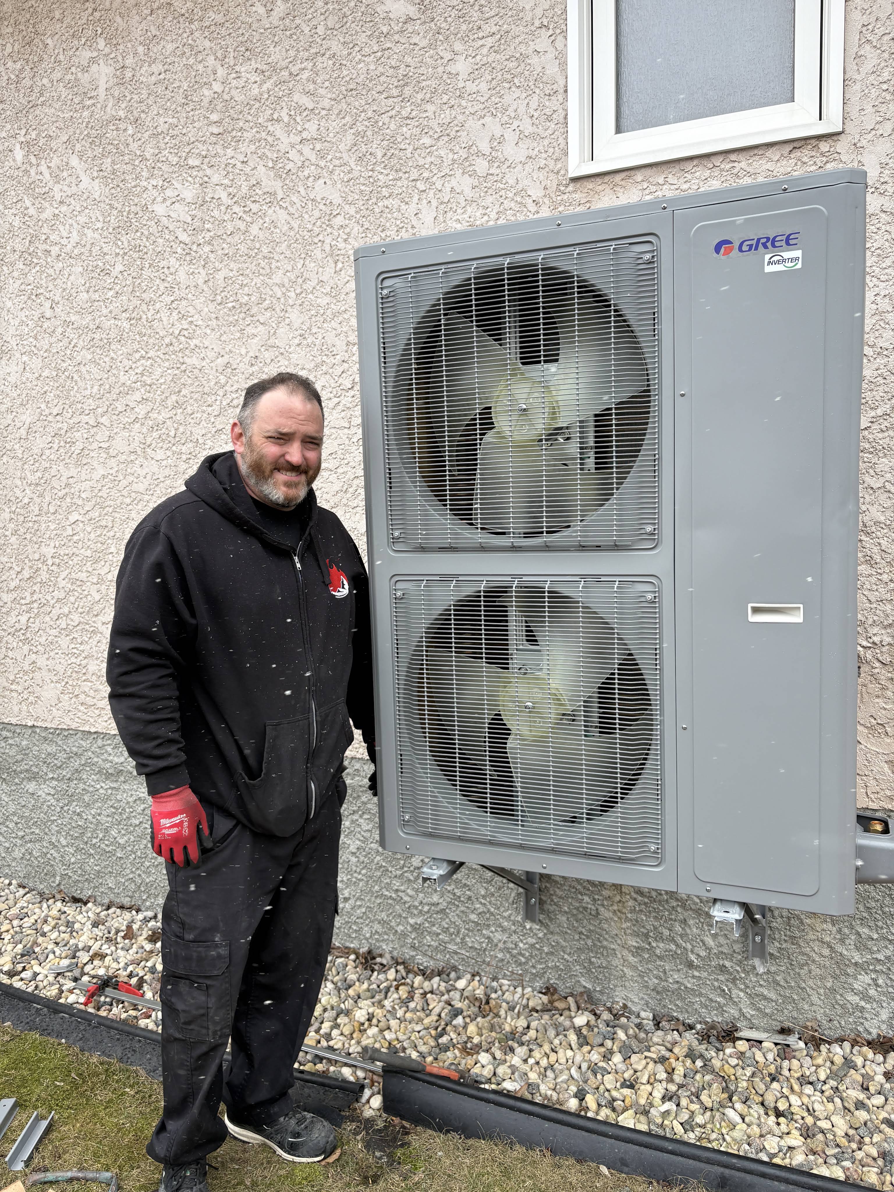 Technician in a Whyte Ridge hoodie standing beside a newly installed dual-fan Gree heat pump