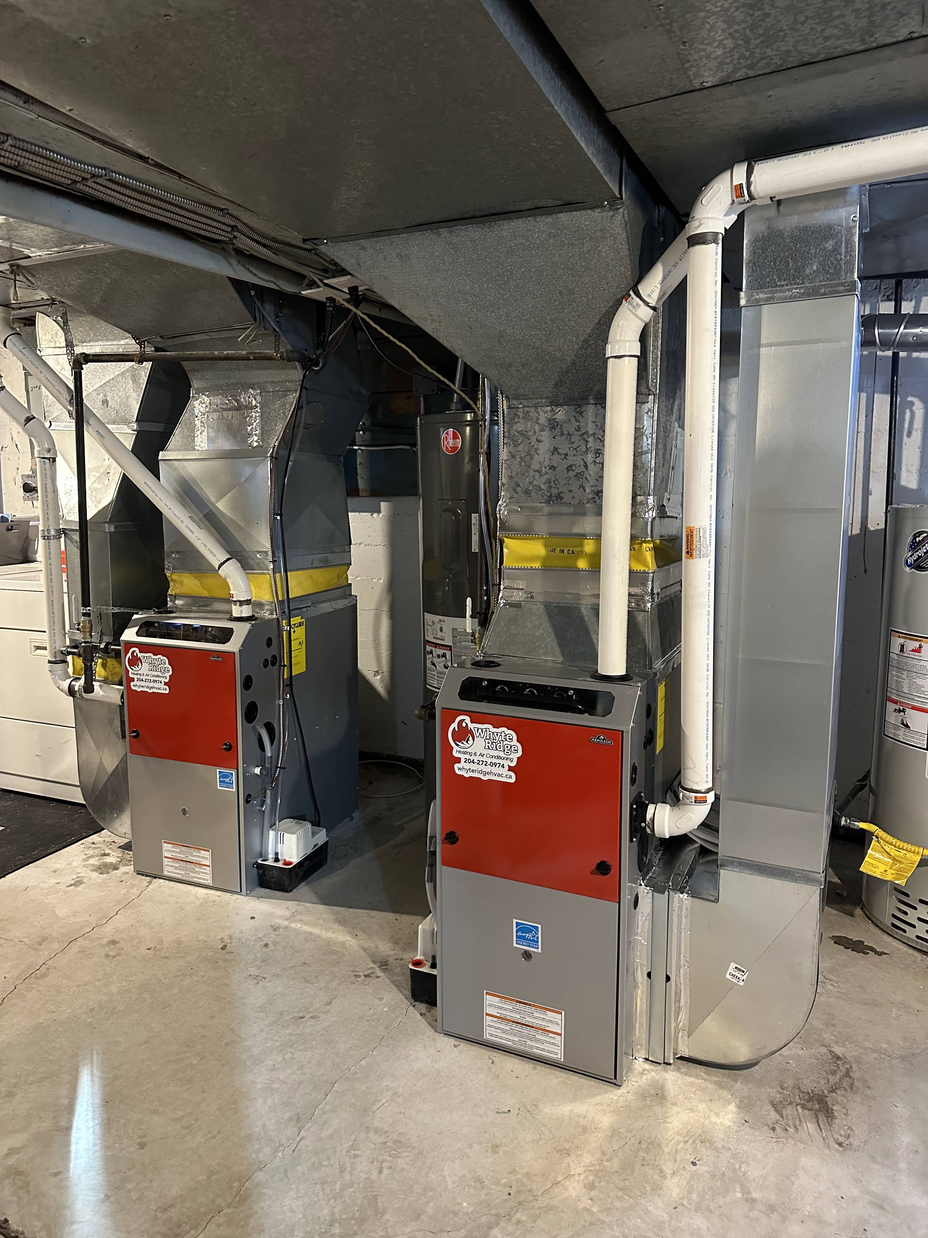 Two high-efficiency gas furnaces installed side by side in a basement mechanical room with new ductwork