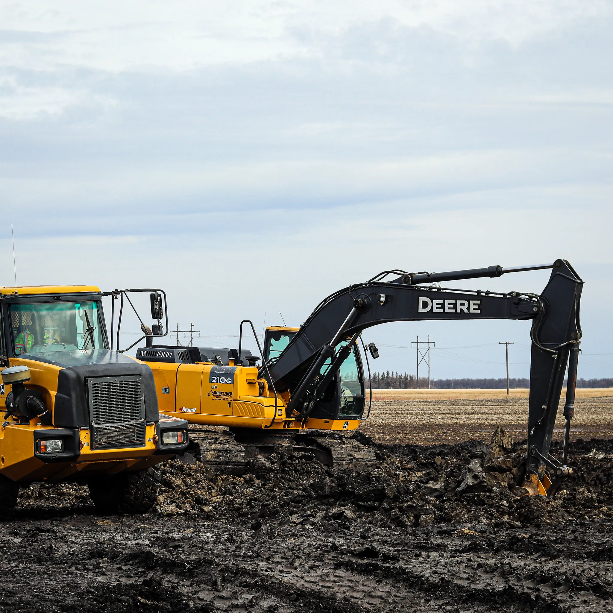 Excavator and articulated dump truck working in a muddy field, part of a land development or drainage project.