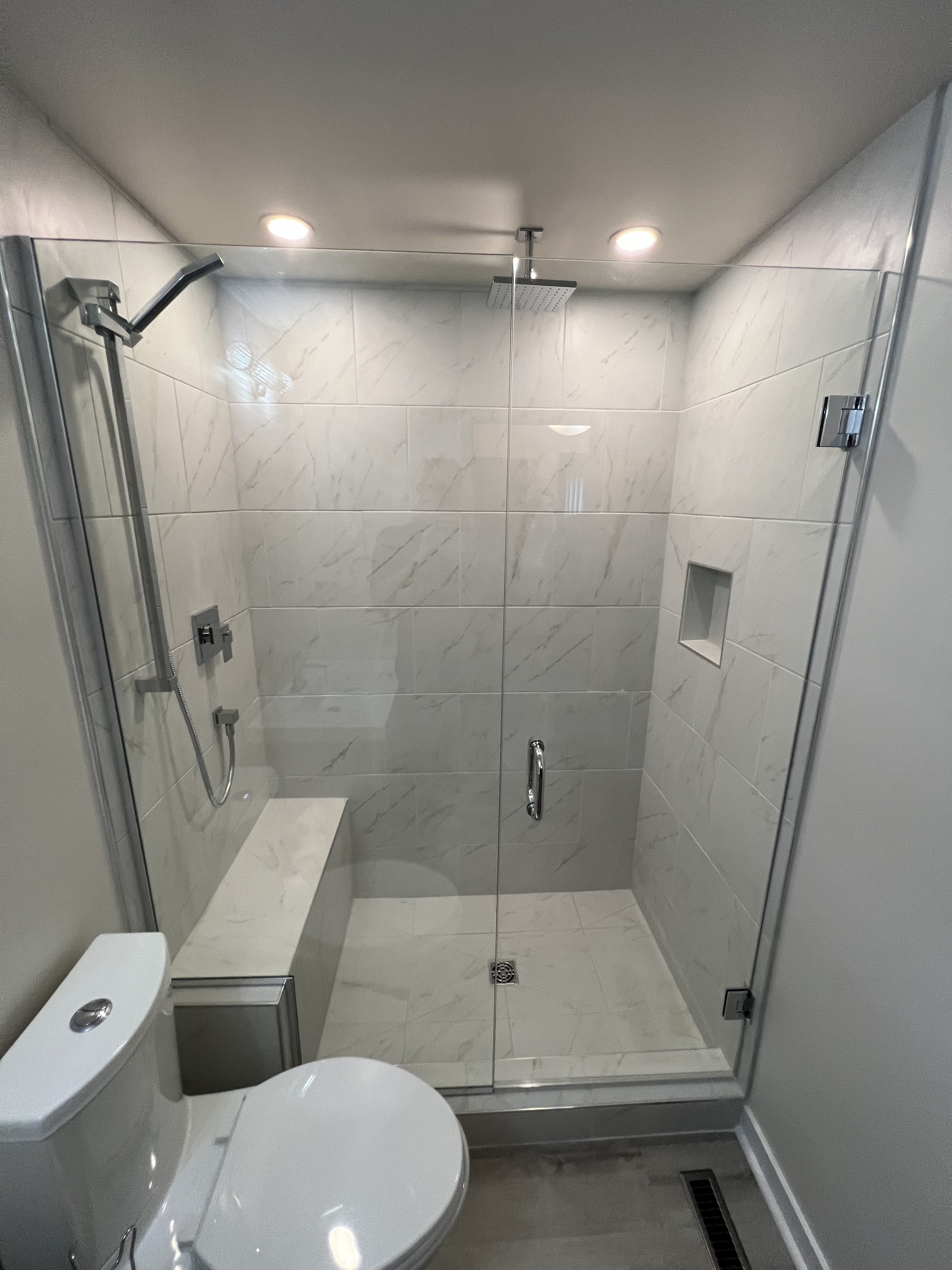 A modern bathroom with a glass-enclosed shower stall featuring a rainfall showerhead, a handheld shower, a built-in nich