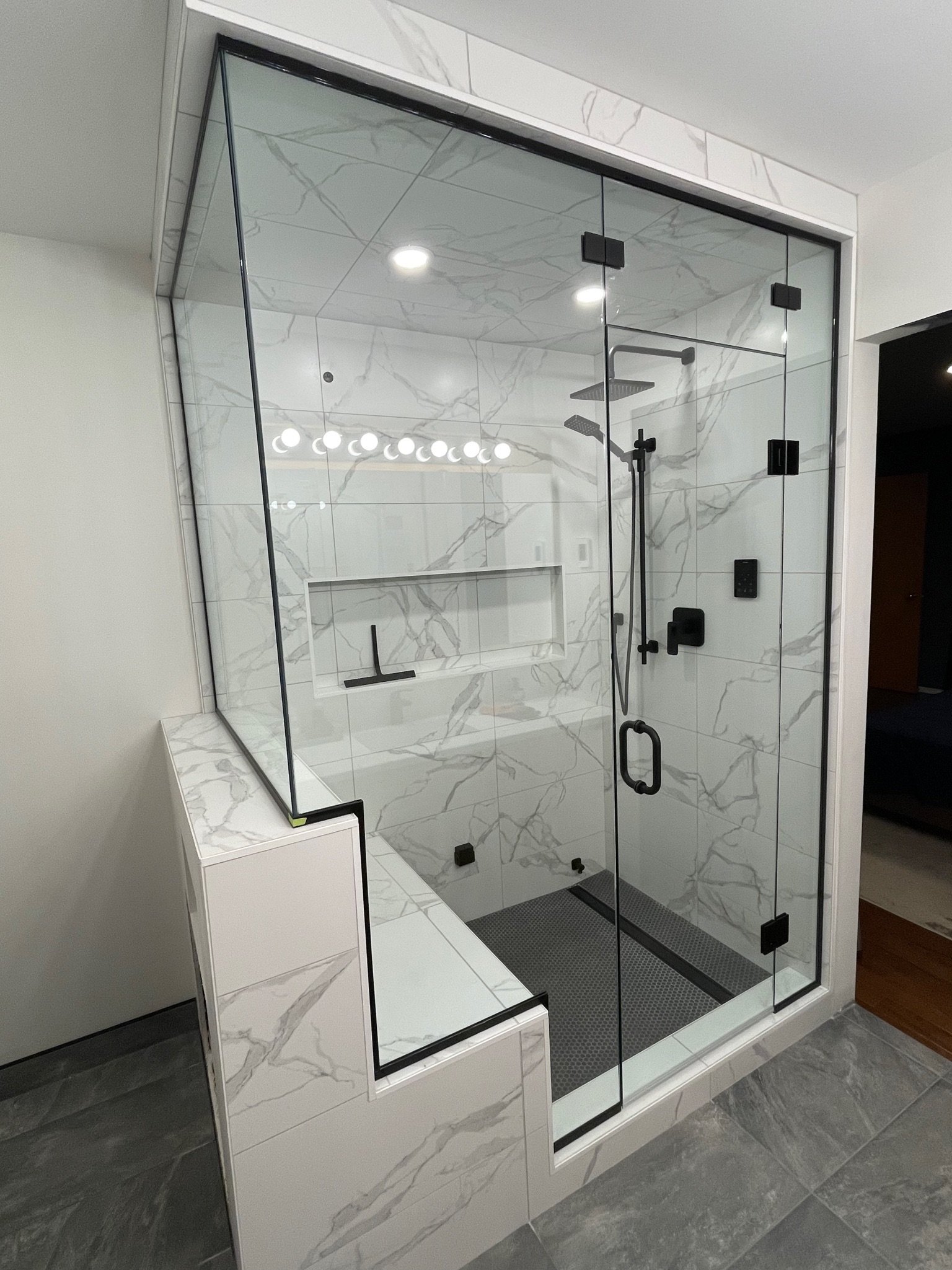Modern walk-in shower with glass walls and marble tiles, black fixtures, and a built-in shower niche.