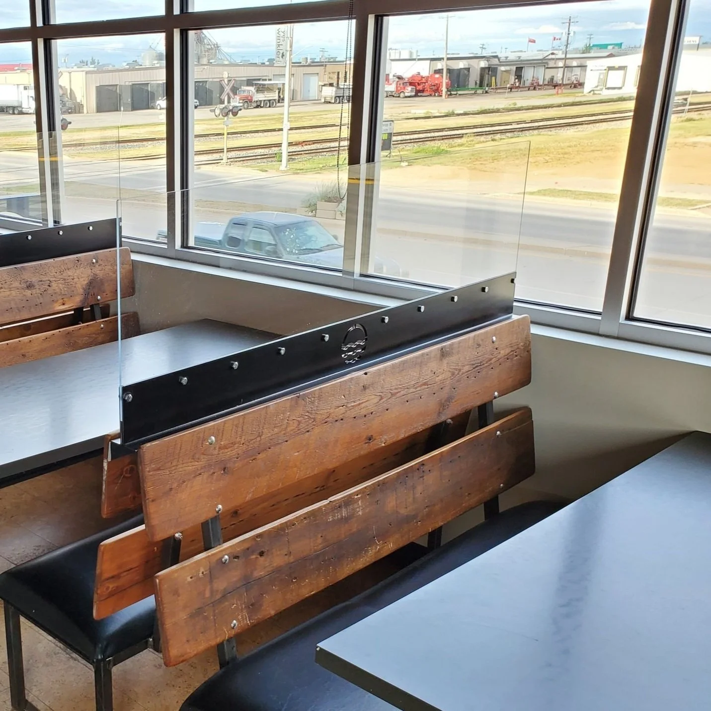 Empty booth with metal framed benches and table in a restaurant, featuring a metal and acrylic divider and large windows