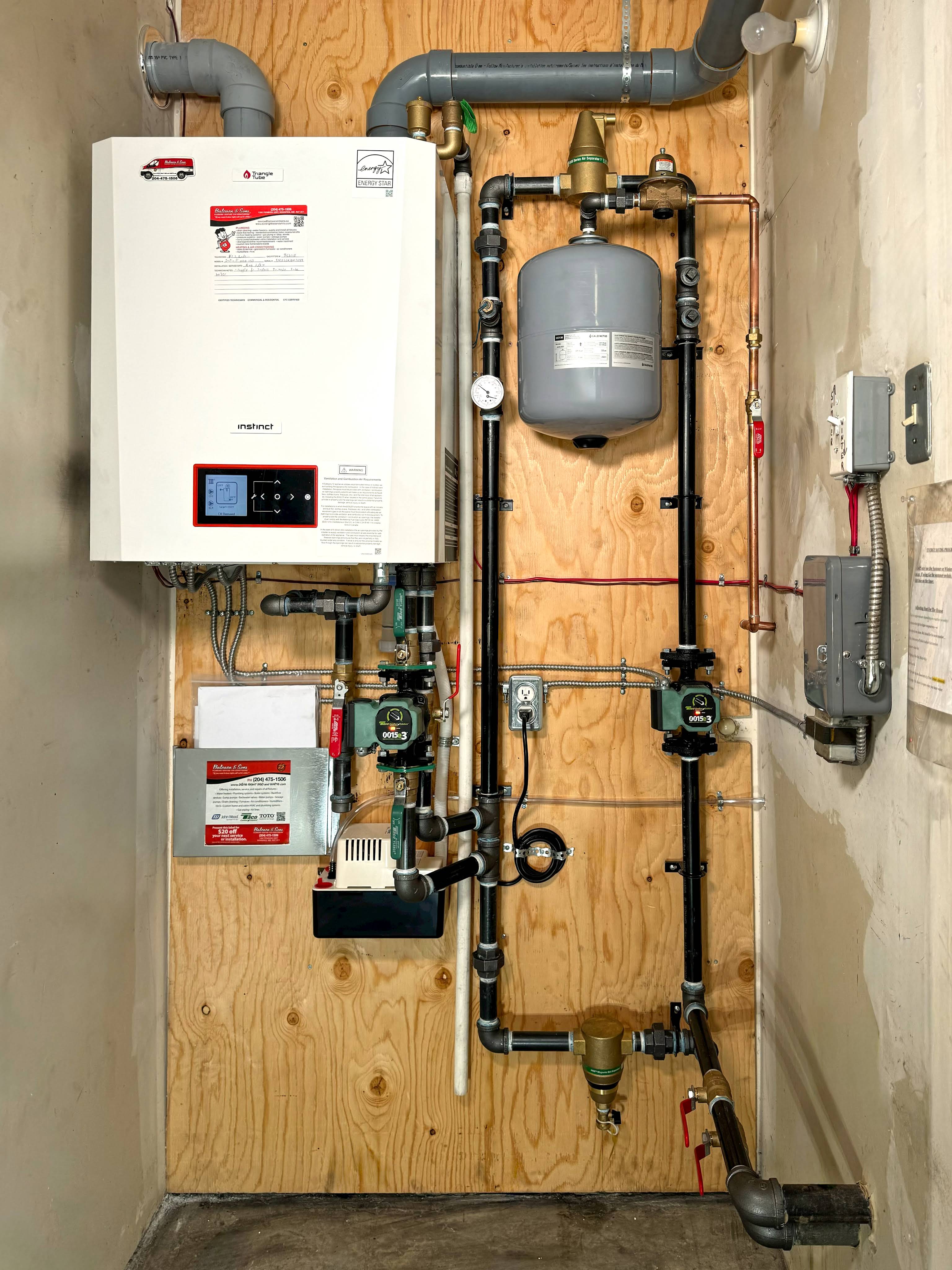 Wall-hung boiler with expansion tank, zone valves and neatly routed vent piping mounted on a plywood board in a mechanical closet