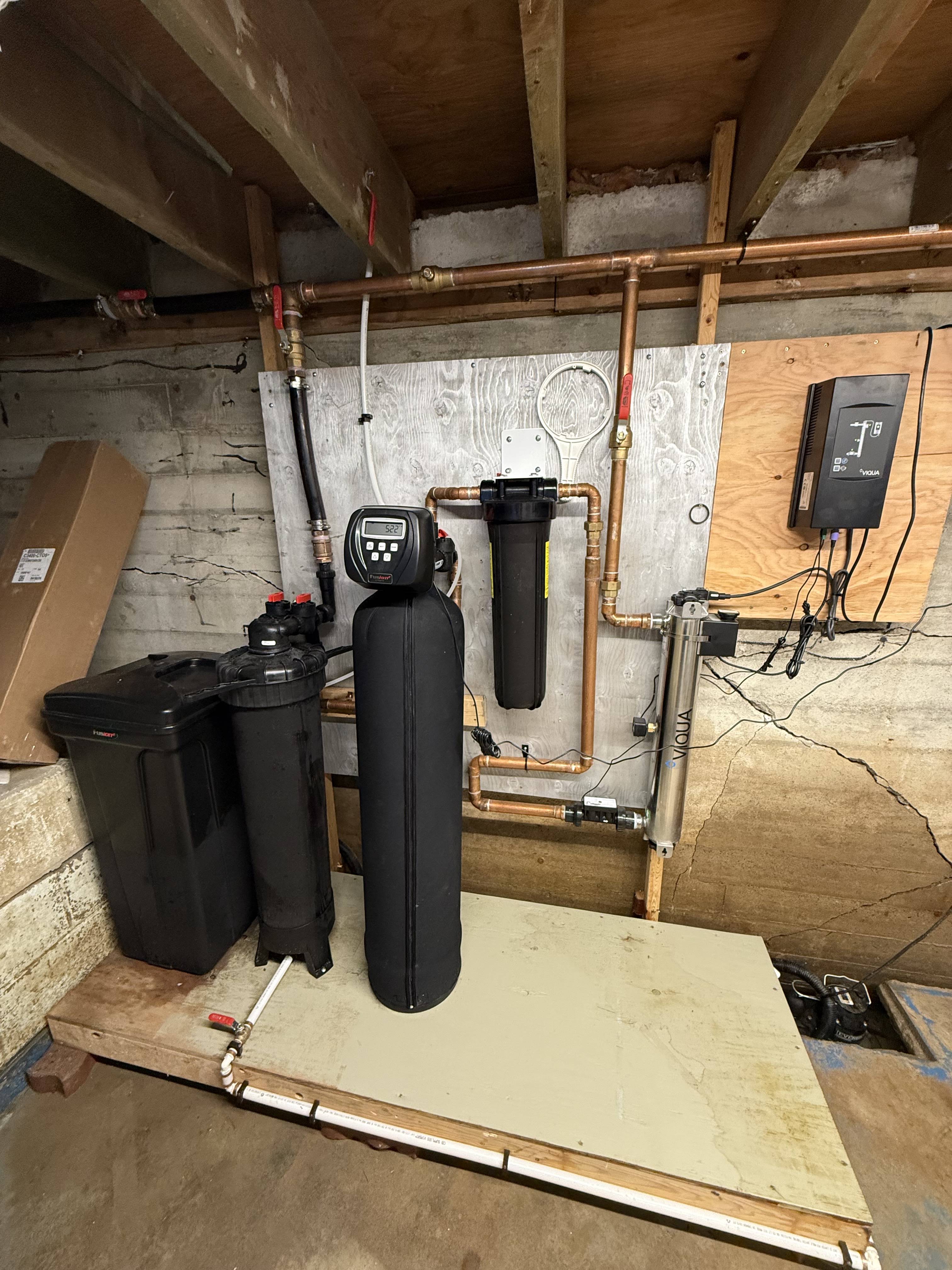 Whole-home water softener, sediment filter and UV treatment system plumbed in copper on a basement wall