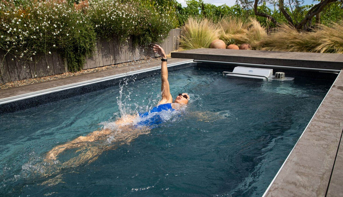 Action shot of the Endless Pools EP510 Modular Pool installed outdoors, surrounded by natural stone decking and lush gre