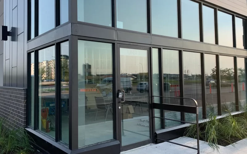 A modern building in Winnipeg showcases large security glass windows with a sleek black frame. A keypad lock secures the